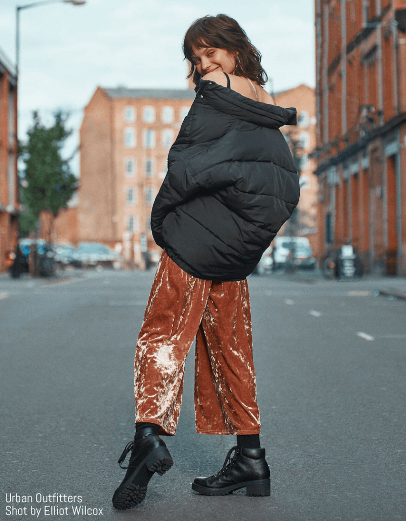 Model poses in hooded puffer coat and velvet pants for Urban Outfitters